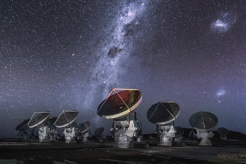 The Atacama Large Millimetre/submillimeter Array (ALMA) antennas work in tandem to form one large telescope. Some of the antennas in this image all point toward the same direction. The brightly shinning Milky Way Galaxy shoots through the sky in the background.
