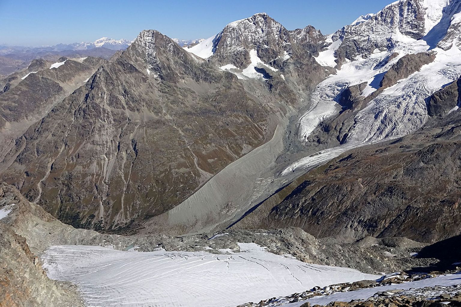 Der Gletscher Vadret da Tschierva im Engadin (September 2016). Der starke Rückgang des Eises zeigt sich eindrücklich in der Bildmitte (Seitenmoränen). Seit 1850 ist gut die Hälfte der Gletschermasse in der Schweiz weggeschmolzen. Der Rückgang des Eises legt Schutt und Geröll frei und lässt neue Seen entstehen – dies verändert die Ästhetik der Landschaft. Falls wir das Klima weiterhin so beeinflussen wie bisher, werden im Jahr 2100 nur noch 20 bis 30% der heutigen Eismassen übrigbleiben. Die Schneesaison wird sich um mehrere Wochen verkürzen und die Schneegrenze um mehrere Hundert Meter ansteigen. Infrastrukturen wie Skilifte, die heute auf Permafrostböden stehen, werden ihren stabilen Untergrund verlieren. Auf dem Jungfraujoch auf rund 3500 m ü. M. schmilzt der Permafrost bereits seit einigen Jahren im Sommer. Der Verlust an Schnee und Felsstabilität wird die (Schnee-) Sicherheit in Bergregionen und den Tourismus beeinträchtigen und zu Anpassungen zwingen. Auch die Pflanzenwelt wird sich anpassen müssen – so droht beispielsweise die Fichte aus dem Mittelland zu verschwinden.